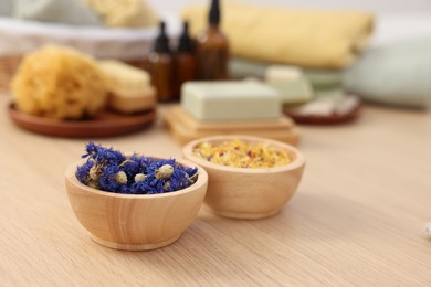 Photo of Bowls with dry flowers on light wooden table, space for text. Spa therapy