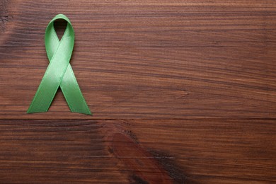 Photo of World Mental Health Day. Green ribbon on wooden background, top view with space for text