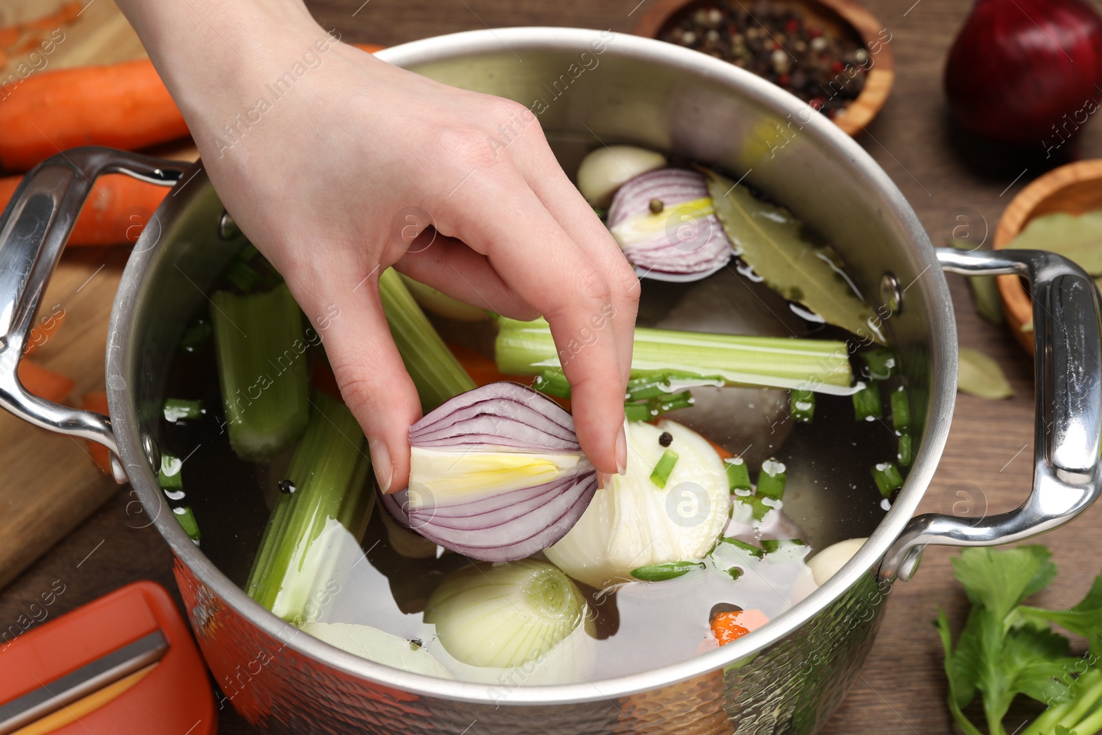 Photo of Cooking tasty bouillon. Woman putting onion into pot with different ingredients at wooden table, closeup