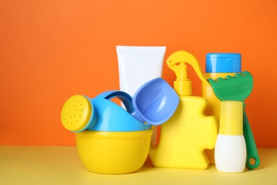 Photo of Different suntan products and plastic beach toys on color background