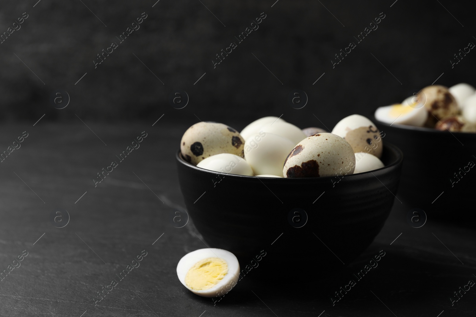 Photo of Unpeeled and peeled hard boiled quail eggs on black table, space for text