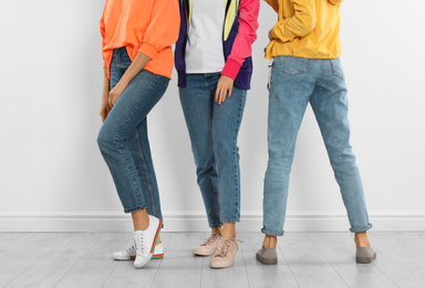 Photo of Group of young women in stylish jeans near white wall, closeup