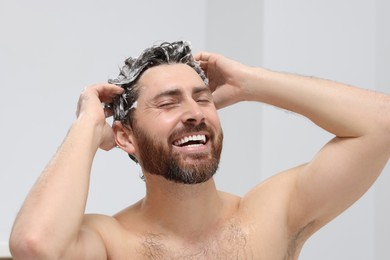 Photo of Happy man washing his hair with shampoo in shower