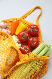 Photo of String bag with different vegetables on light grey background, top view