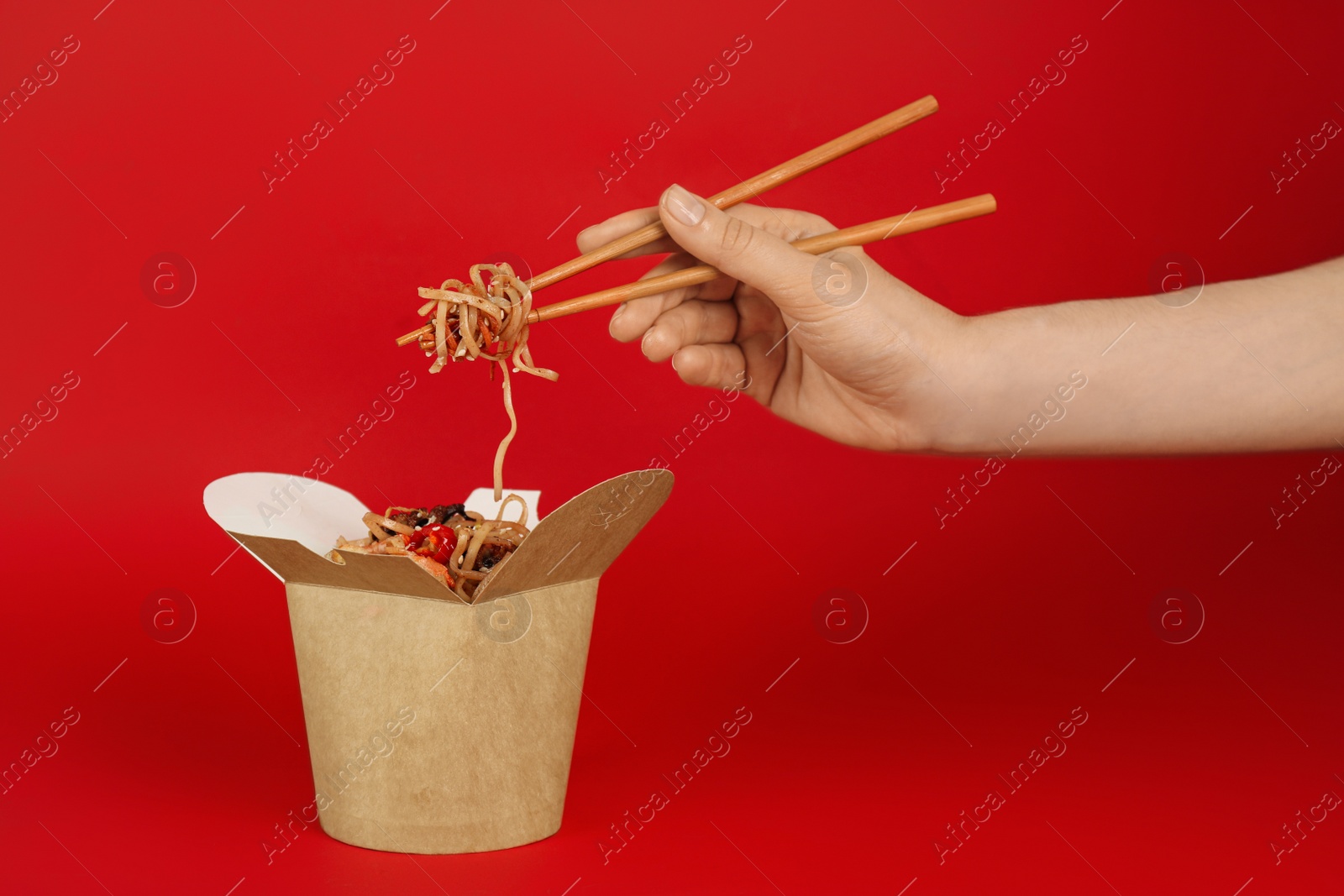 Photo of Woman eating seafood wok noodles with chopsticks from box on red background, closeup