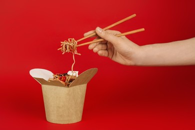 Woman eating seafood wok noodles with chopsticks from box on red background, closeup