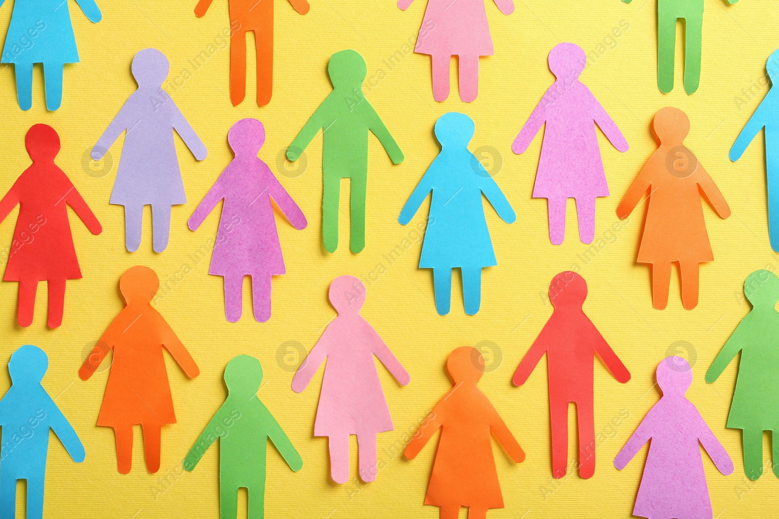 Photo of Many different paper human figures on yellow background, flat lay. Diversity and inclusion concept