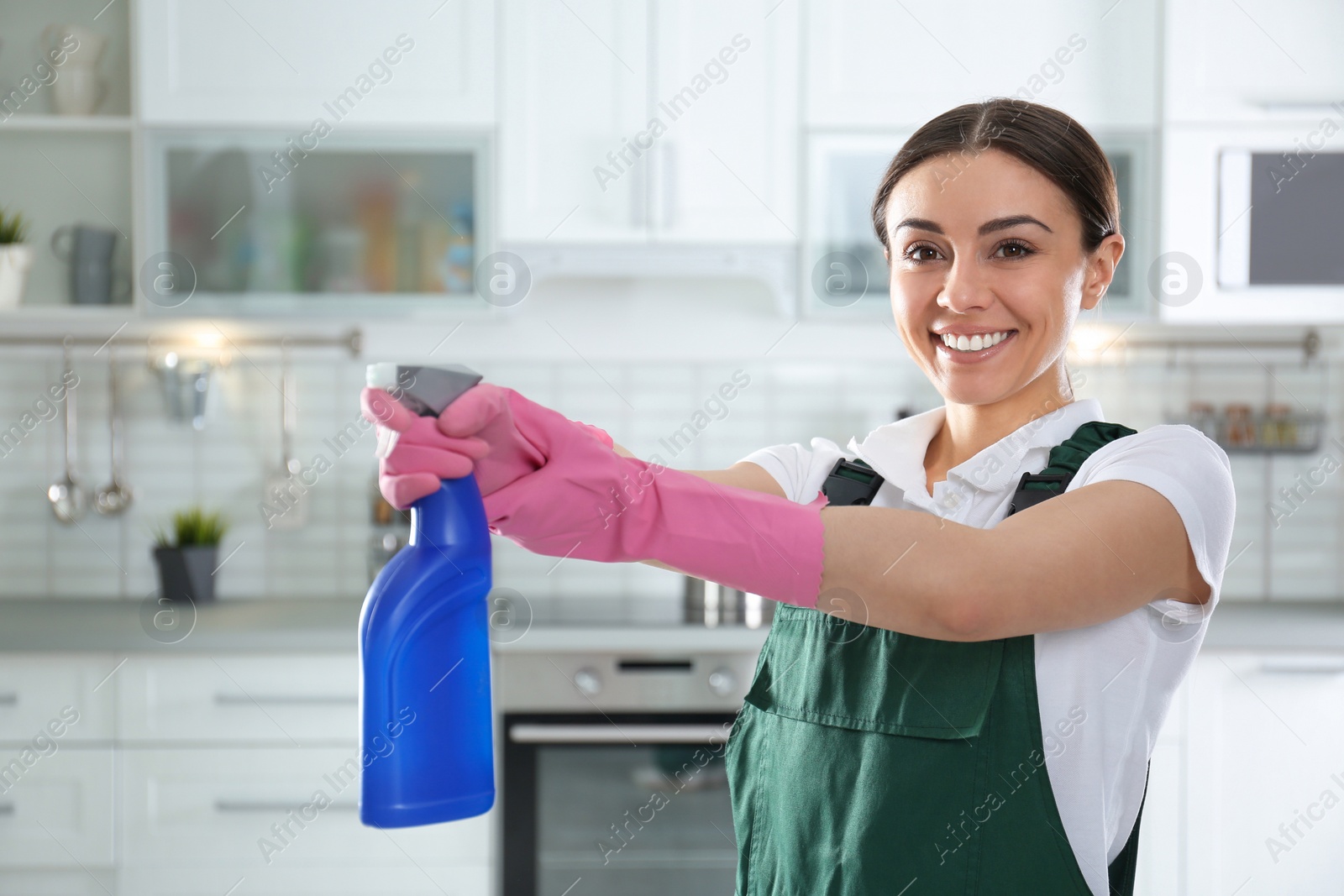 Photo of Portrait of young woman with sprayer in kitchen. Cleaning service