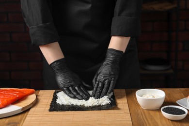Photo of Chef in gloves making sushi roll at wooden table, closeup
