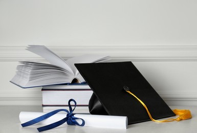 Photo of Graduation hat, books and diploma on floor near white wall