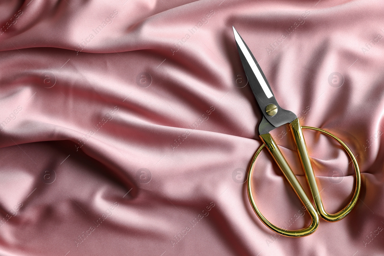 Photo of Scissors on silk fabric, top view. Space for text