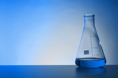 Image of Conical flask with liquid on table, space for text. Toned in blue. Laboratory glassware