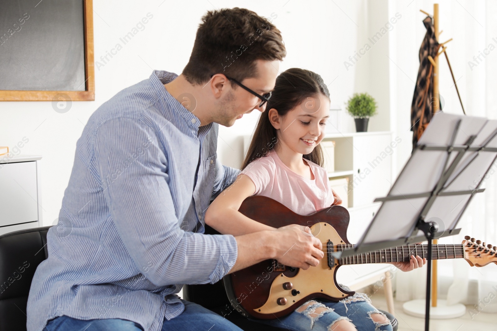 Photo of Little girl playing guitar with her teacher at music lesson. Learning notes