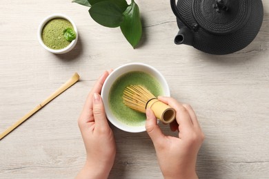 Woman preparing matcha tea with bamboo whisk at wooden table, top view