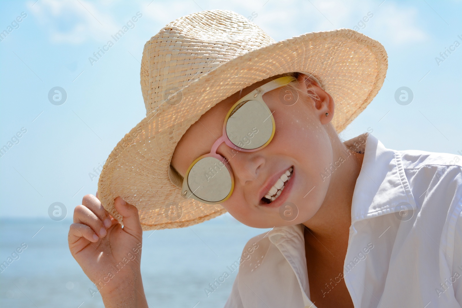 Photo of Little girl wearing sunglasses and hat at beach on sunny day