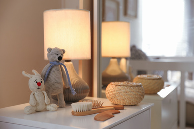 Toys, lamp and hair brushes on chest of drawers near mirror indoors. Interior elements