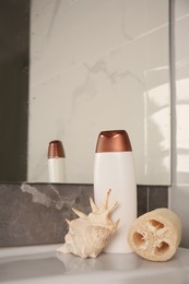 Natural loofah sponge, seashell and bottle of shower gel on washbasin in bathroom, space for text