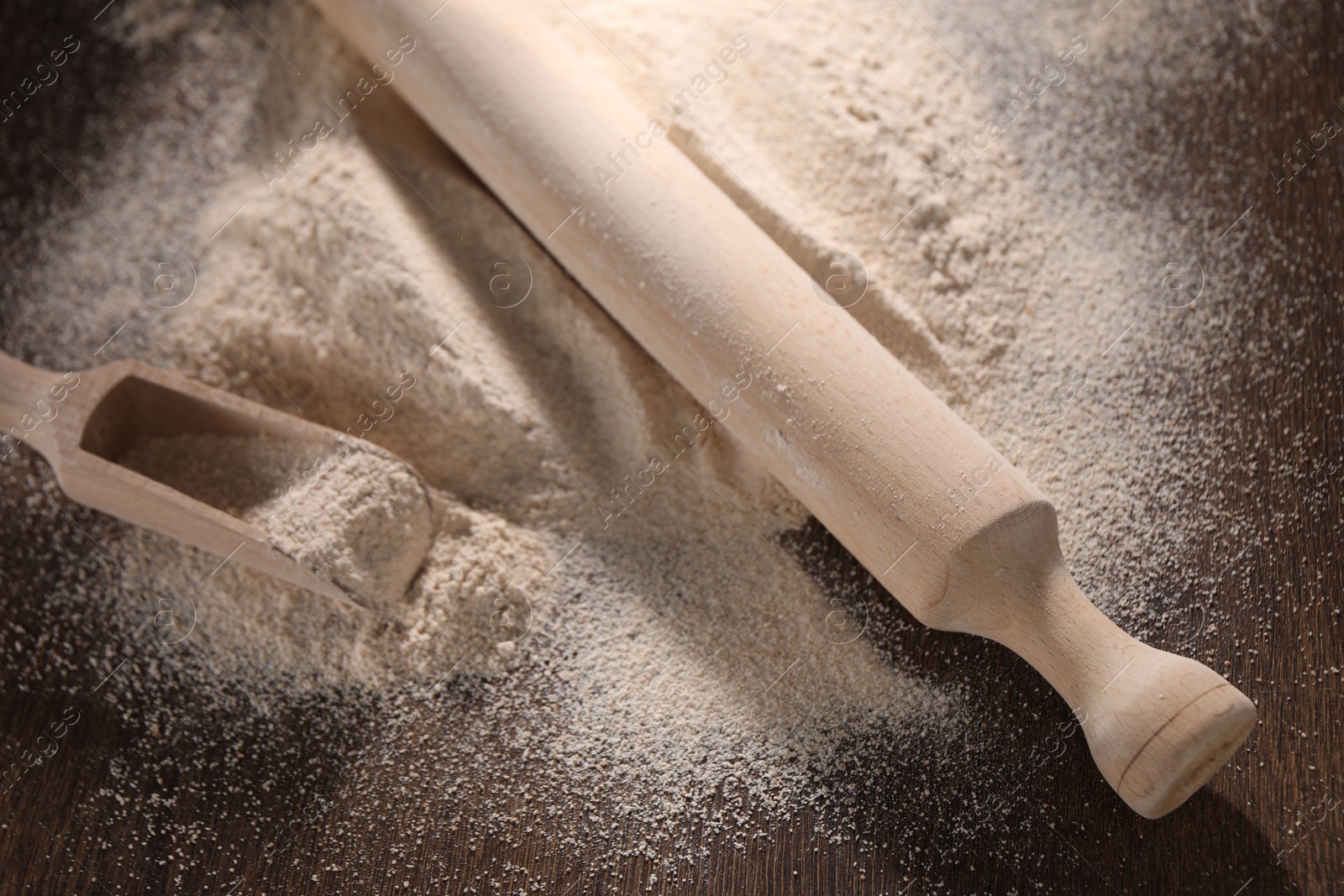 Photo of Pile of flour, rolling pin and scoop on wooden table, closeup