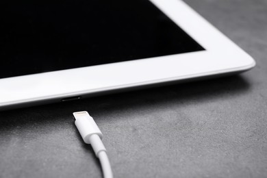 USB cable with lightning connector and tablet on dark table, closeup
