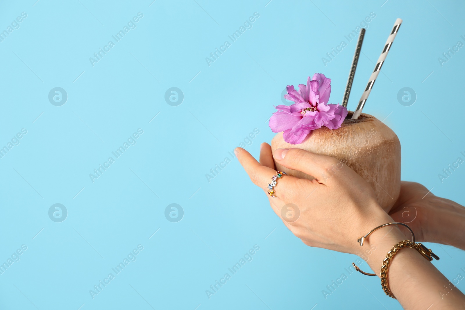 Photo of Woman holding fresh young coconut with straws on light blue background, closeup. Space for text