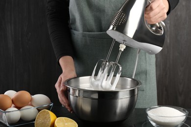 Photo of Woman making whipped cream with hand mixer at black table, closeup