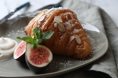 Delicious croissant with fig, almond flakes and cream on table, closeup