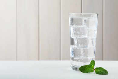 Glass of soda water with ice and mint on white table. Space for text