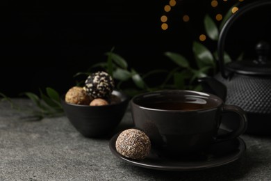 Photo of Cup of aromatic tea and delicious vegan candy balls on grey table against blurred lights, space for text