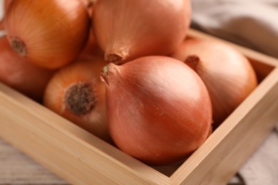 Crate with ripe onions on white wooden table, closeup