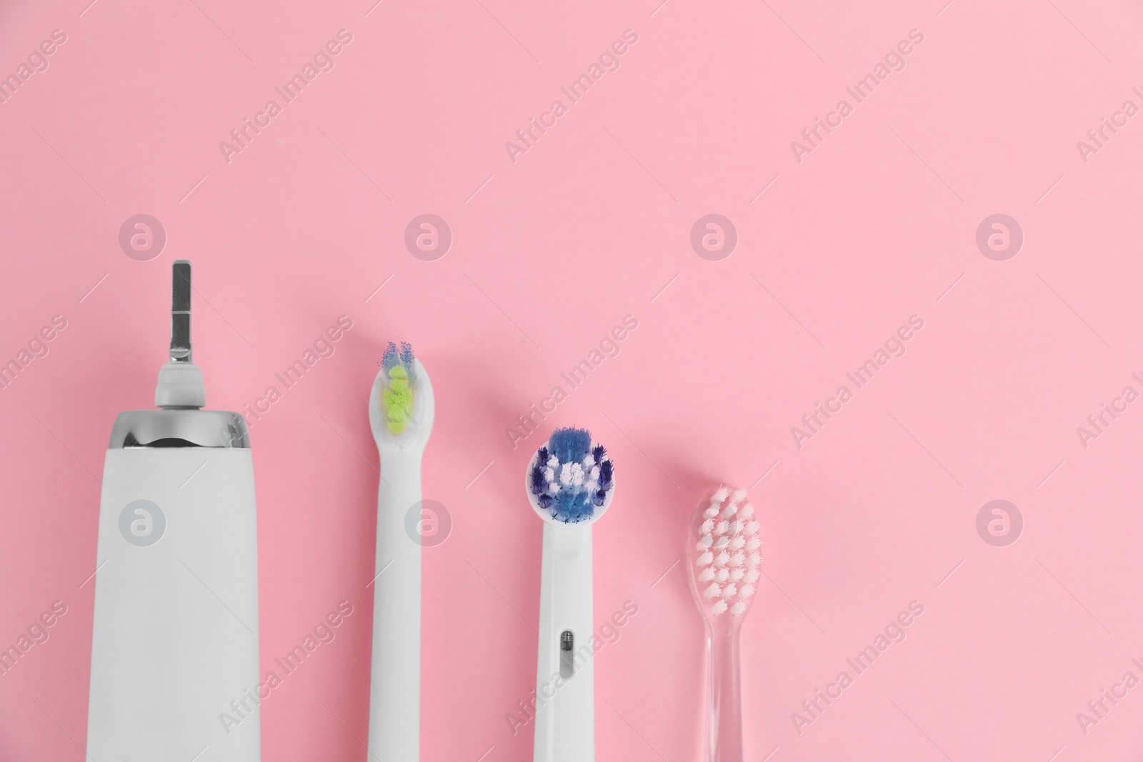 Photo of Electric toothbrush and replacement brush heads on pink background, flat lay. Space for text