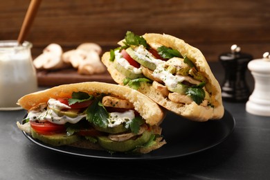 Photo of Delicious pita sandwiches with grilled vegetables and sour cream sauce on black textured table, closeup