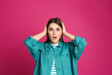 Portrait of shocked young woman on pink background