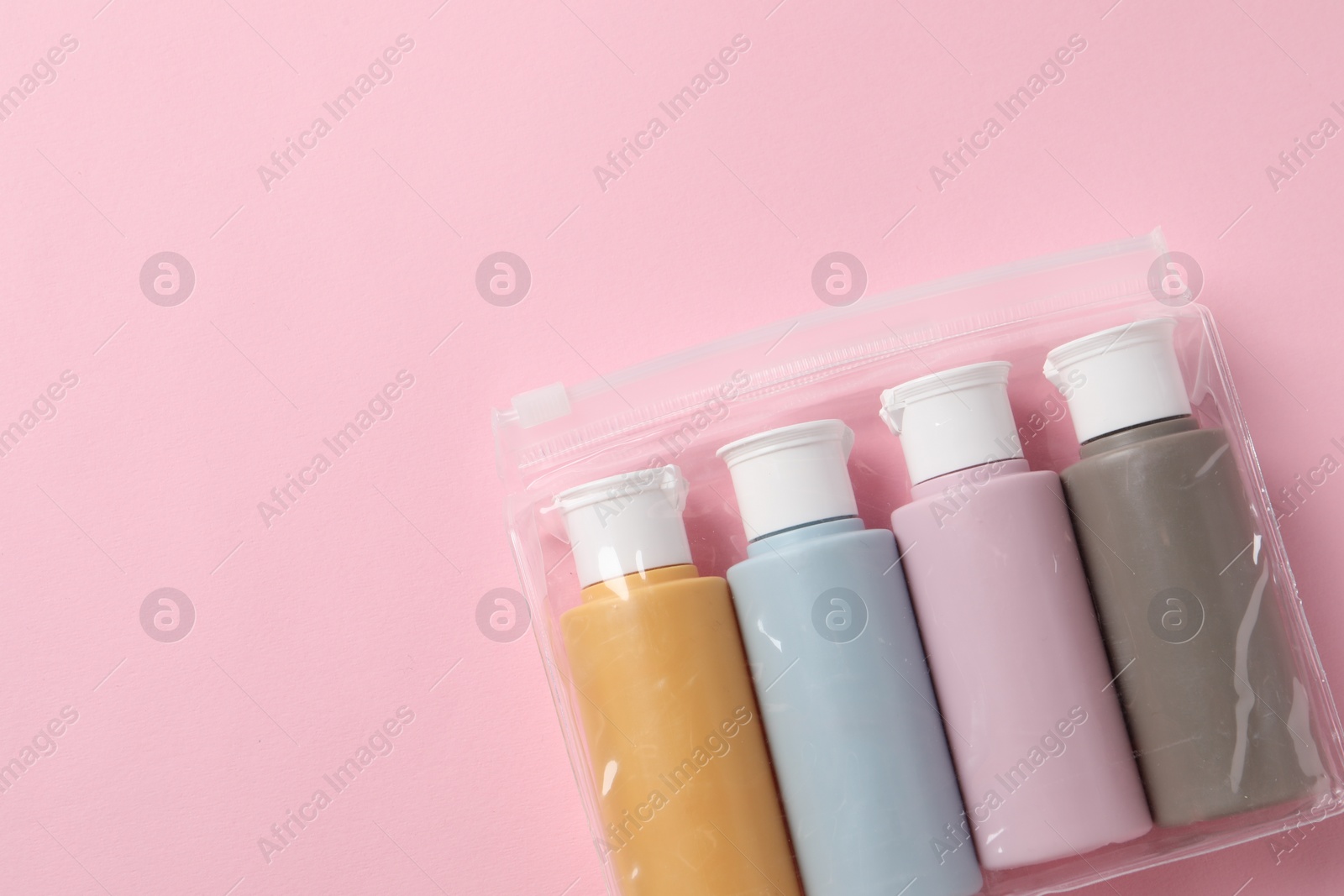 Photo of Cosmetic travel kit in plastic bag on pink background, top view. Space for text