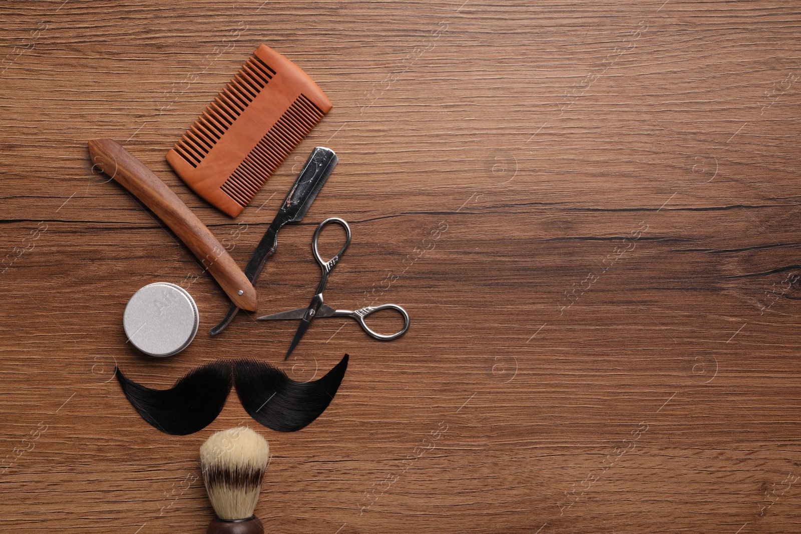 Photo of Artificial moustache and barber tools on wooden table, flat lay. Space for text