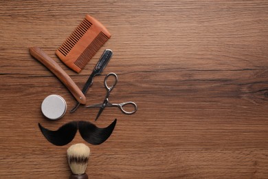 Photo of Artificial moustache and barber tools on wooden table, flat lay. Space for text