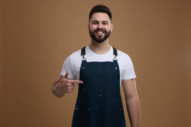 Photo of Smiling man pointing at kitchen apron on brown background. Mockup for design