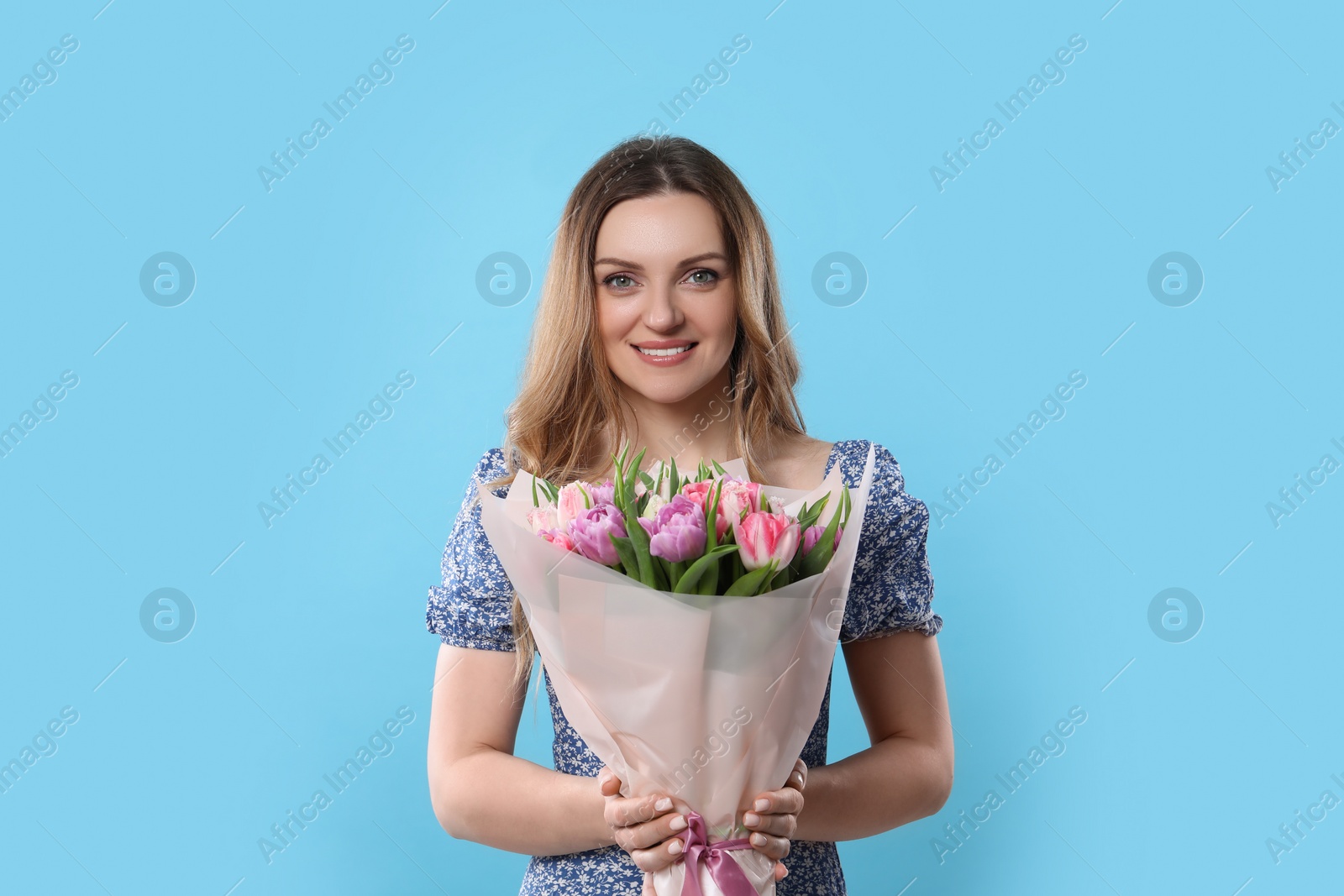 Photo of Happy young woman with bouquet of beautiful tulips on light blue background