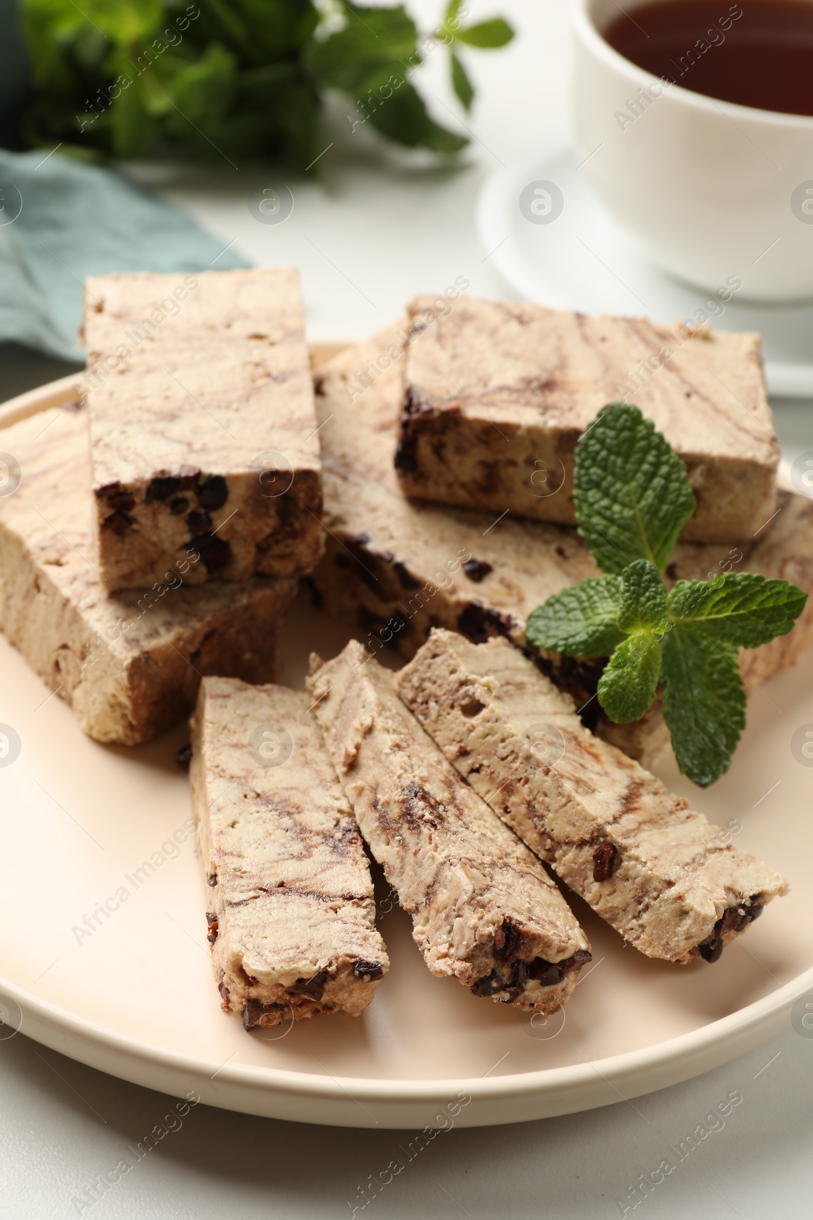 Photo of Pieces of tasty chocolate halva and mint on white table, closeup