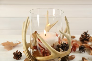 Photo of Stylish holder with burning candle and autumn decor on white wooden table, closeup