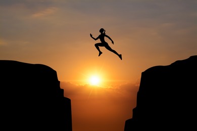 Image of Concept of reaching life and business goals. Silhouette of woman jumping over chasm at sunrise