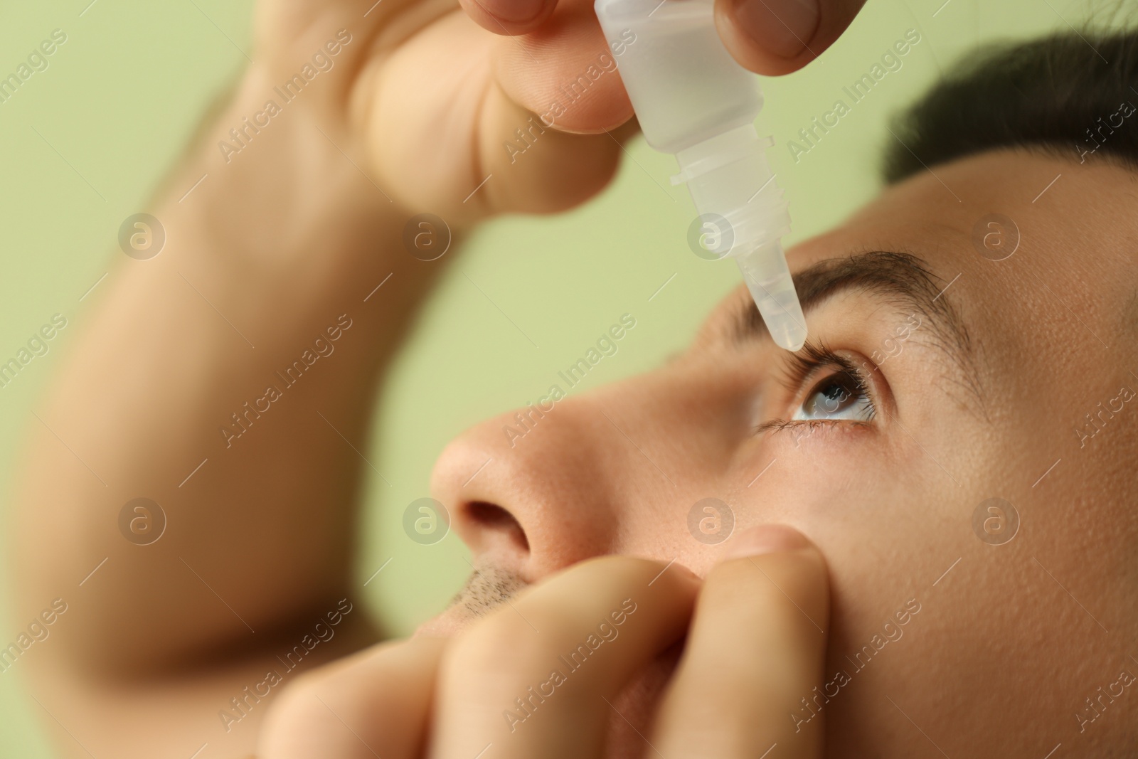 Photo of Man using eye drops on green background, closeup