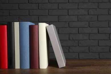 Many different hardcover books on wooden table near dark brick wall, space for text