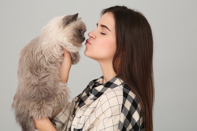 Woman kissing her cute cat on light grey background