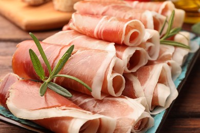 Photo of Rolled slices of delicious jamon with rosemary on table, closeup
