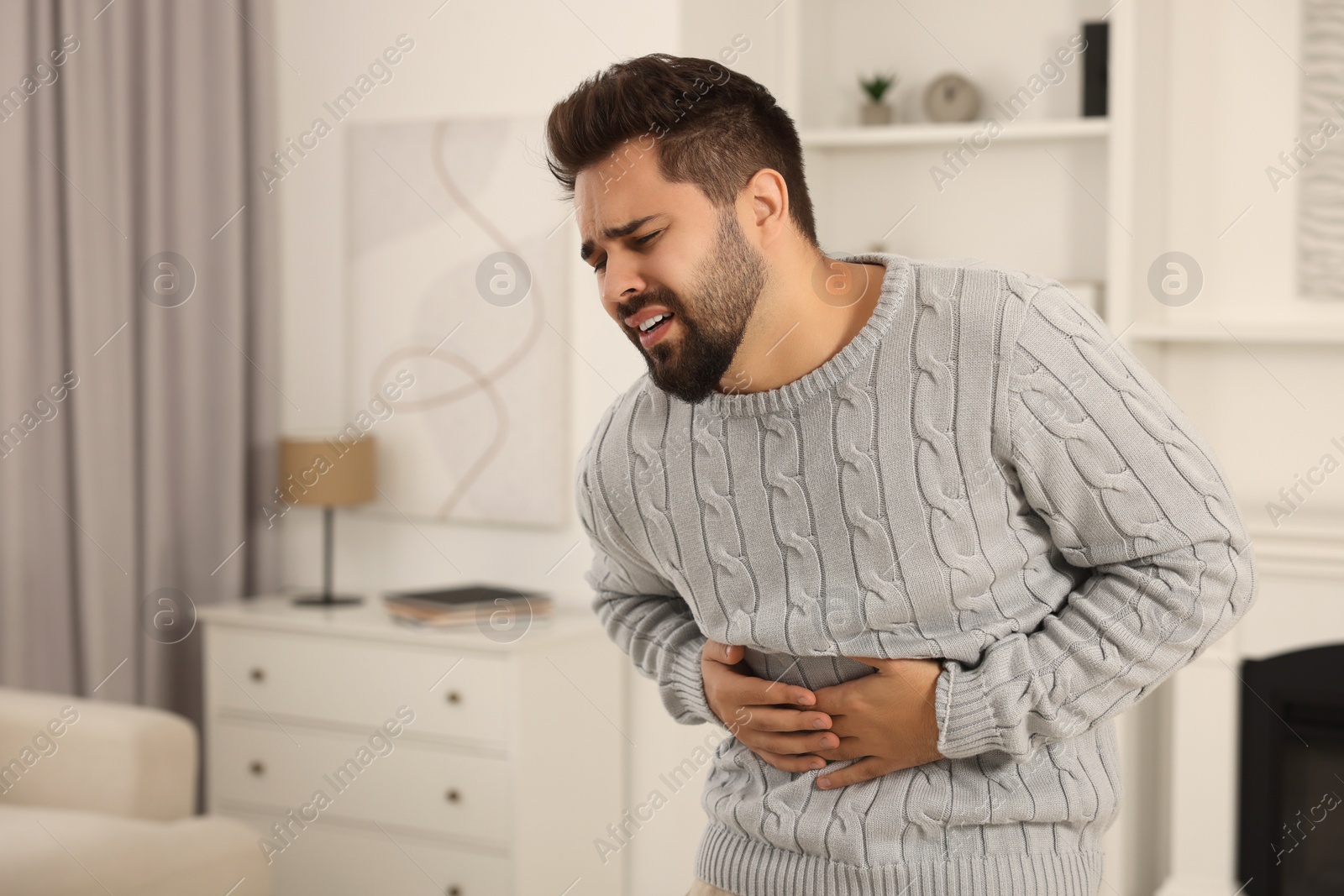 Photo of Young man suffering from stomach pain indoors. Space for text