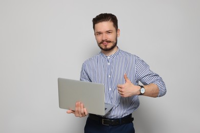 Smiling man with laptop showing thumbs up on light grey background