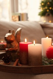 Photo of Tray with beautiful burning candles and Christmas decor on sofa at home, closeup