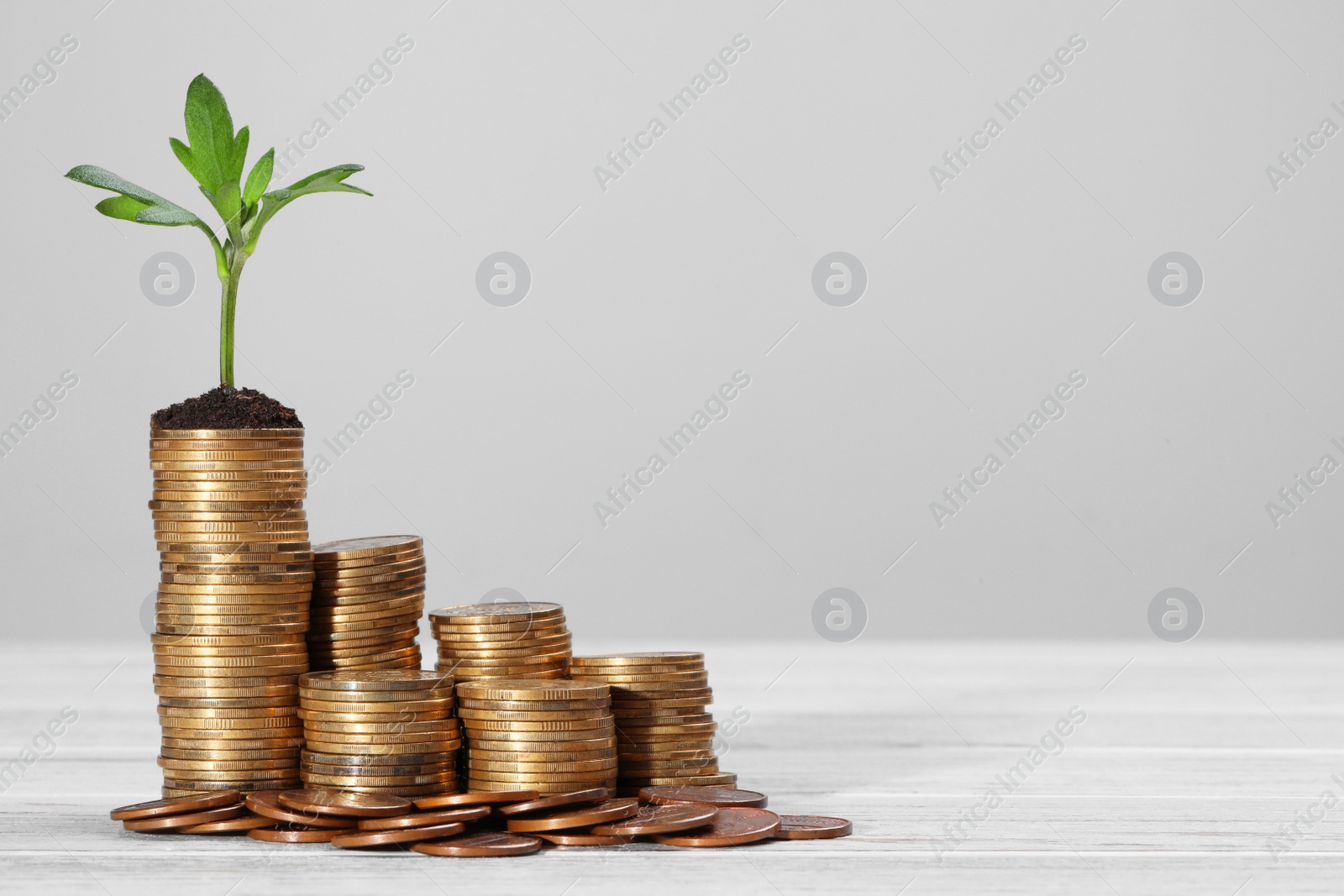 Photo of Stacks of coins and green sprout on white wooden table against light grey background, space for text. Investment concept
