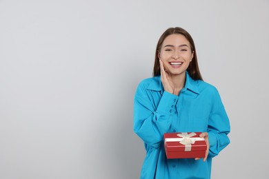 Photo of Portrait of emotional young woman with gift box on grey background. Space for text