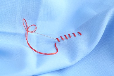 Photo of Sewing needle with thread and stitches on light blue cloth, closeup